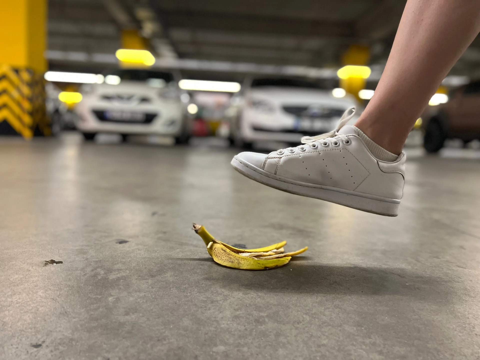 White sneaker stepping over a banana peel on a smooth car park floor — the slip risk of an uncoated deck.
