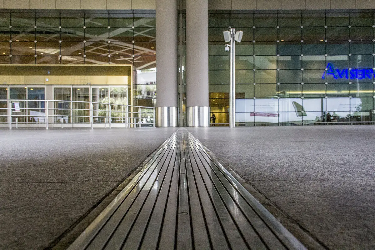 Metallic expansion joint cover installed across a polished terminal floor in front of a glass curtain wall