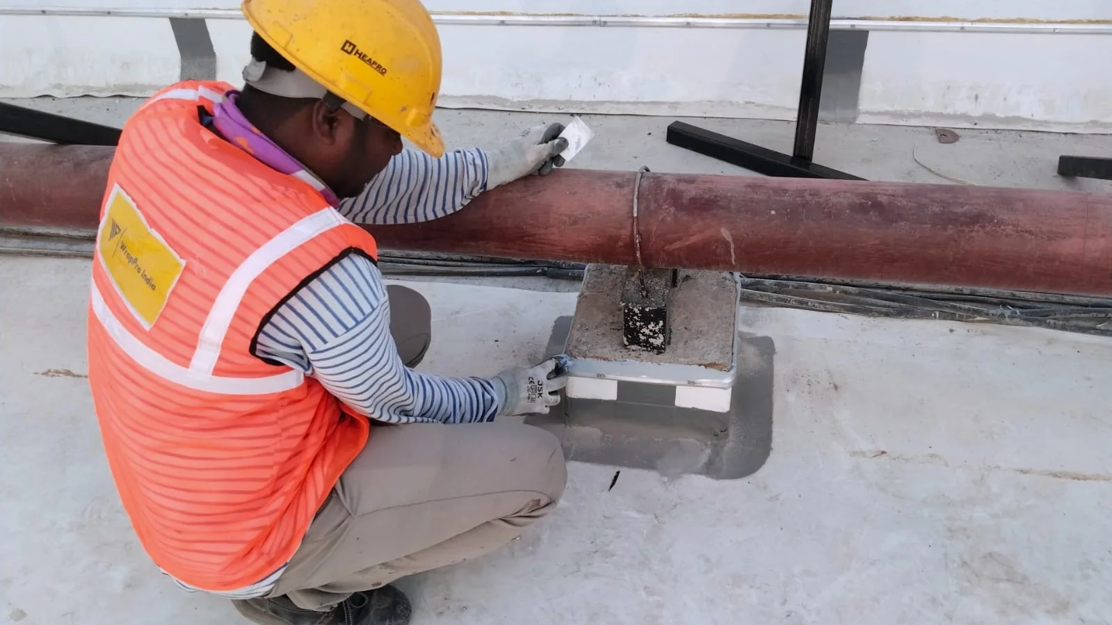 WrapPro technician detailing waterproofing at a pipe support junction on a white terrace