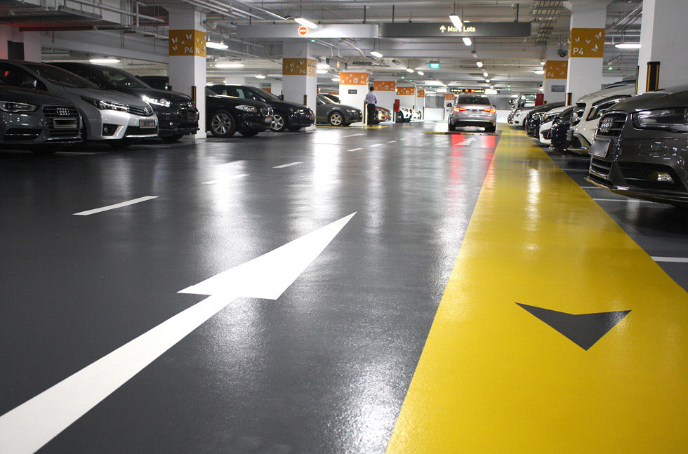Indoor car park deck with coated grey flooring, yellow circulation lane and white directional arrows