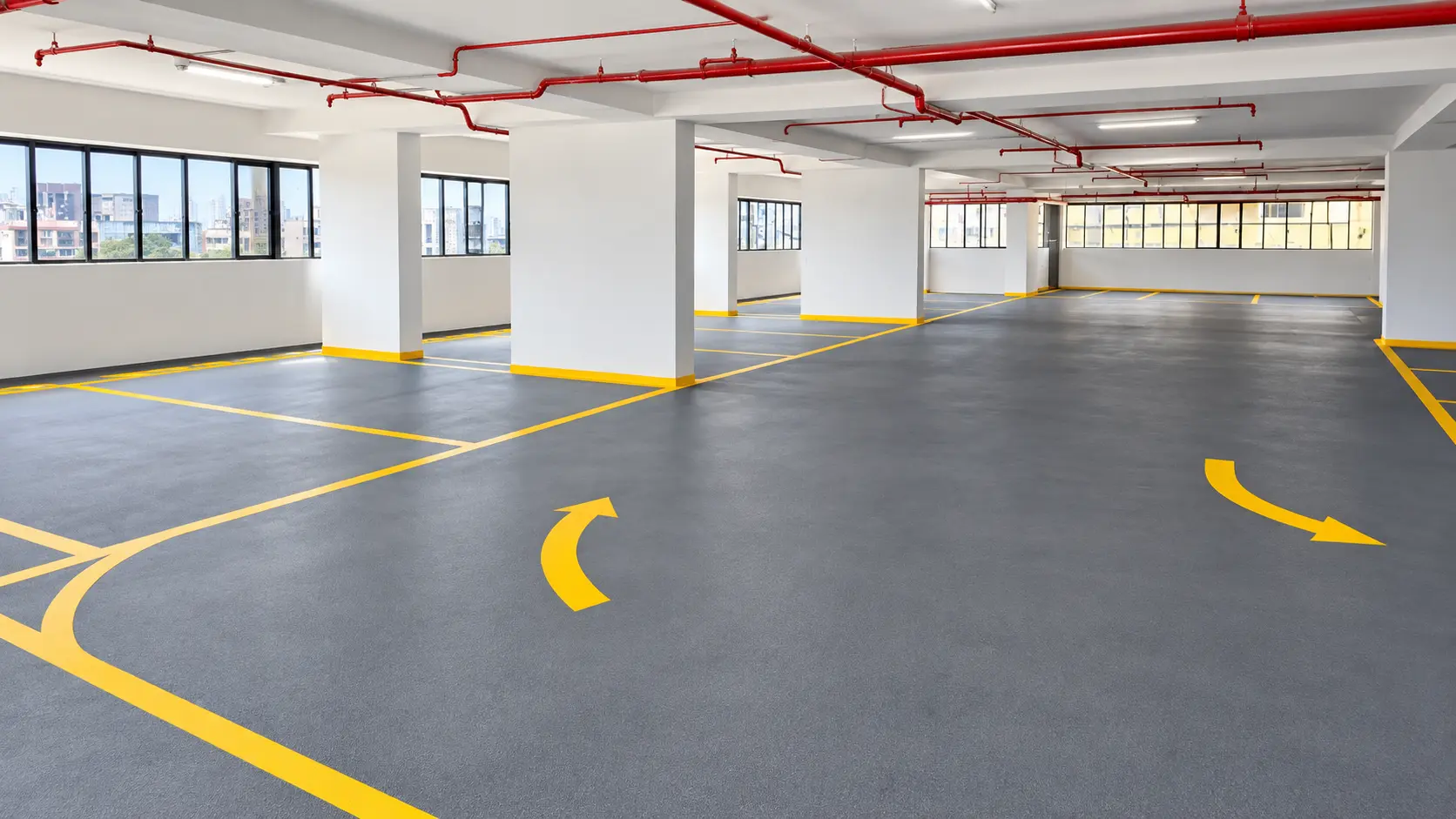 Clean parking garage interior with a smooth dark grey floor marked with bright yellow arrows and lines