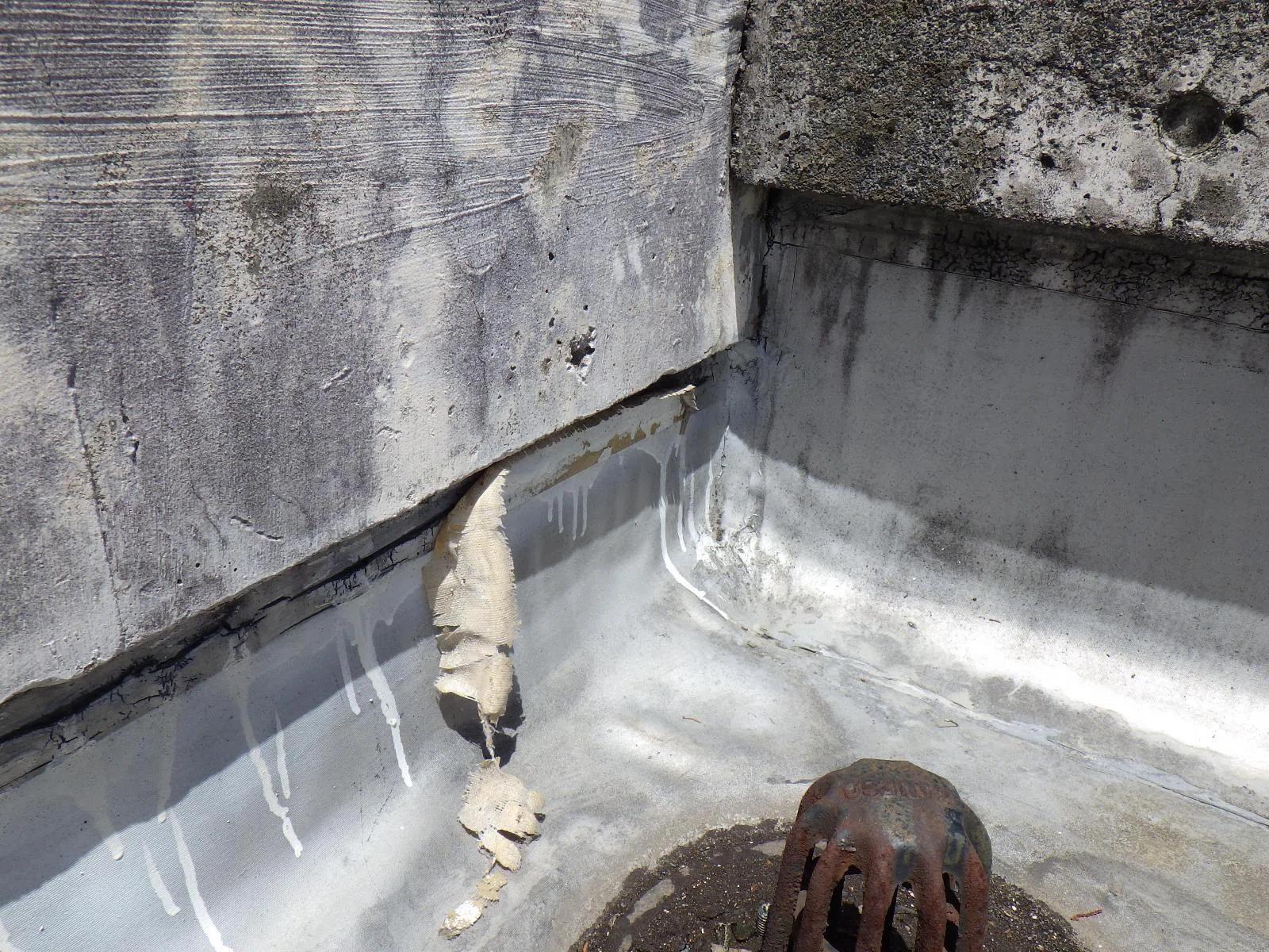 A poorly detailed roof waterproofing system, with the membrane peeling away at the parapet junction beside the outlet