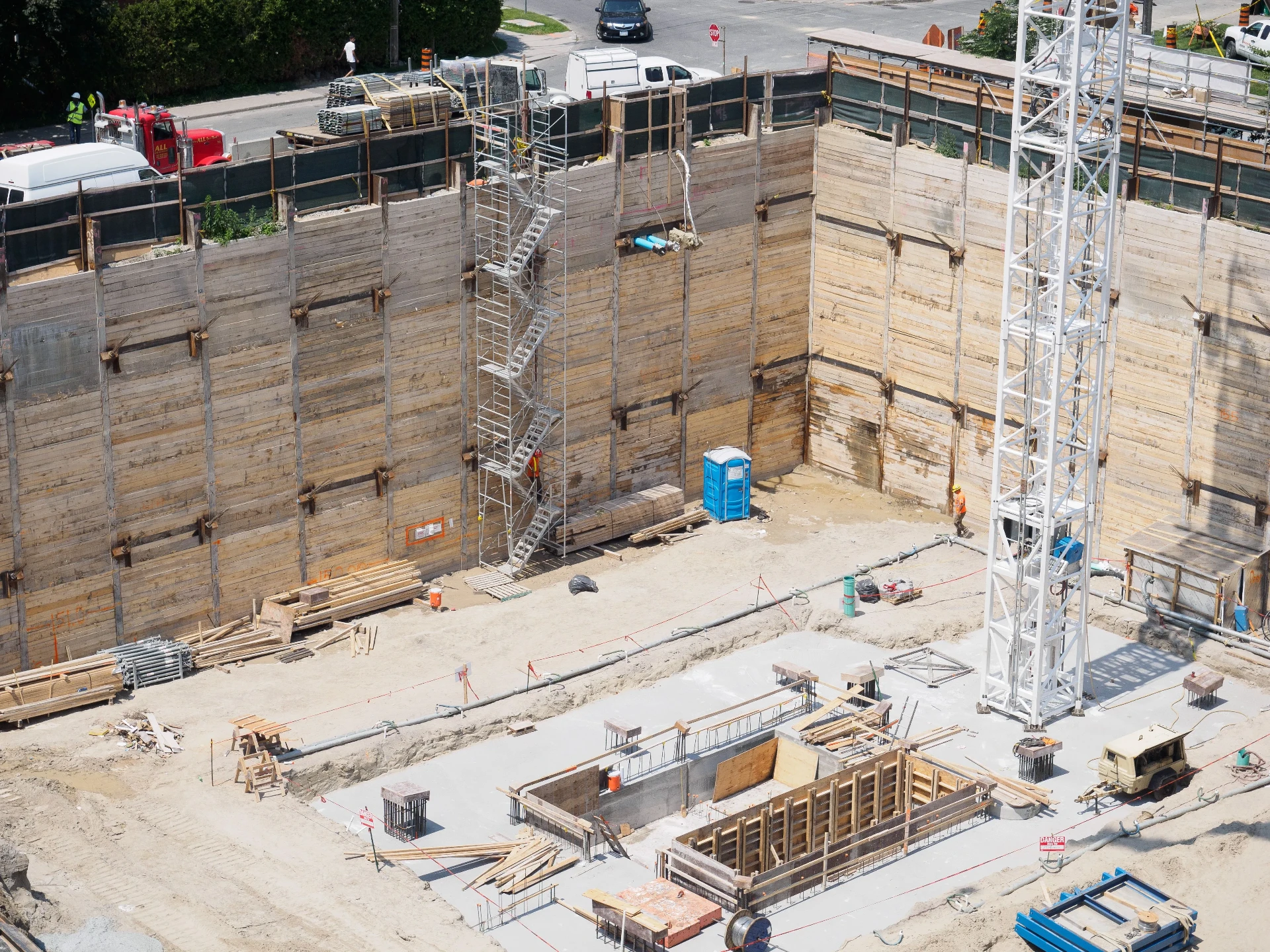 Aerial view of a deep basement excavation with shoring walls on an active building site